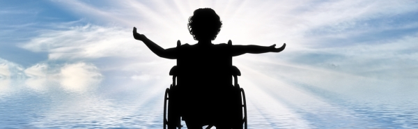 Silhouette of someone in a wheelchair facing a light. Their arms are stretched wide.
